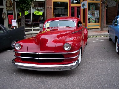 1972 Ford Ranchero - A bright red coupe with extensive chrome detailing is parked on a street next to another vehicle.