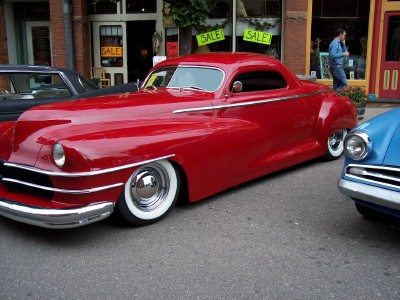1972 Ford Ranchero - A bright red custom coupe with chrome accents and whitewall tires is parked on a street with other vehicles and storefronts.