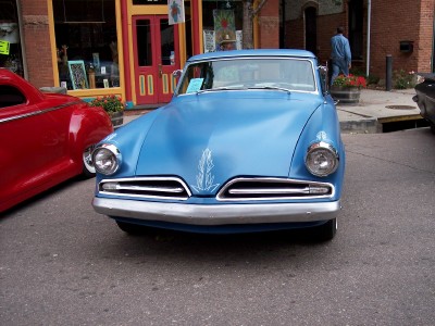 1972 Ford Ranchero - A blue Studebaker sedan is parked on a street in front of a building with red doors.