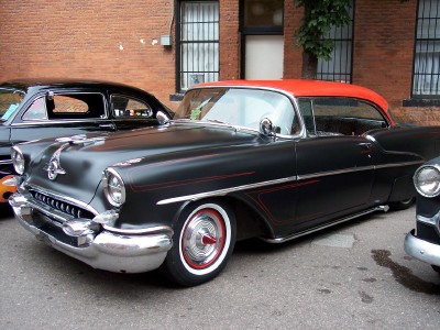 1972 Ford Ranchero - Black 1955 Oldsmobile with red roof and pinstripes, parked next to another car.