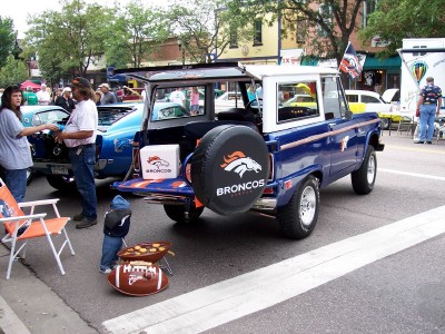 1972 Ford Ranchero - A blue Ford Bronco is parked on a street with its tailgate open, displaying team merchandise.