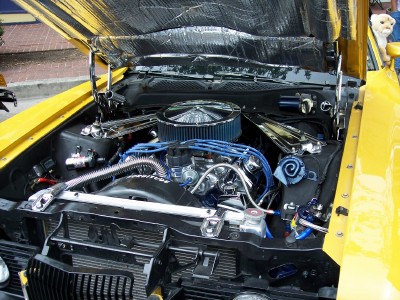 1972 Ford Ranchero - The engine bay of a yellow vehicle is shown with the hood open, revealing the motor and various components.