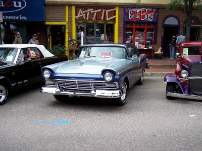 1972 Ford Ranchero - A light blue and blue 1957 Ford Fairlane coupe is parked on a street in front of shops.
