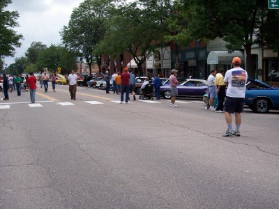 1972 Ford Ranchero - A street is lined with parked cars and onlookers, suggesting a local car show or event.