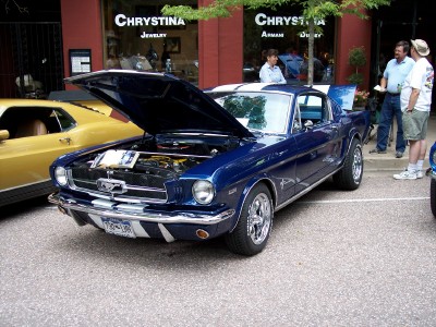 1972 Ford Ranchero - A blue 1965 Ford Mustang is displayed with its hood open, parked on a street in front of a jewelry store.
