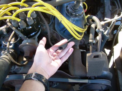1971 Ford F-100 - A hand holds a spark plug wire boot near the distributor and engine block.