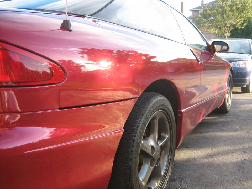 Red 1993 Ford Probe rear quarter panel and wheel, with another vehicle behind