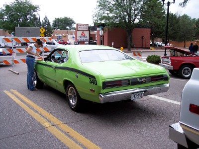1972 Ford Ranchero - A lime green muscle car with a black stripe and '340' emblem is parked on a street with yellow lines, next to other vehicles.