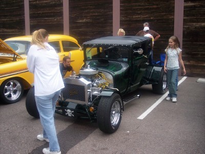1972 Ford Ranchero - A dark green hot rod is parked next to a yellow car, with people observing.