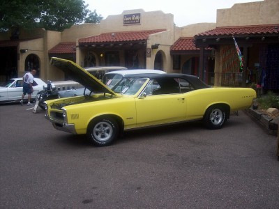 1972 Ford Ranchero - A yellow convertible is parked outside a building with its hood open, alongside another vehicle.