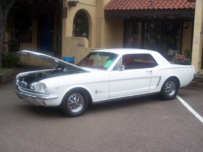 1972 Ford Ranchero - A classic white Ford Mustang is parked with its hood up in front of a building with Spanish-style architecture.