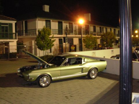 1995 Ford Taurus - A classic green Ford Mustang Fastback is parked outside a building at night with its hood open.