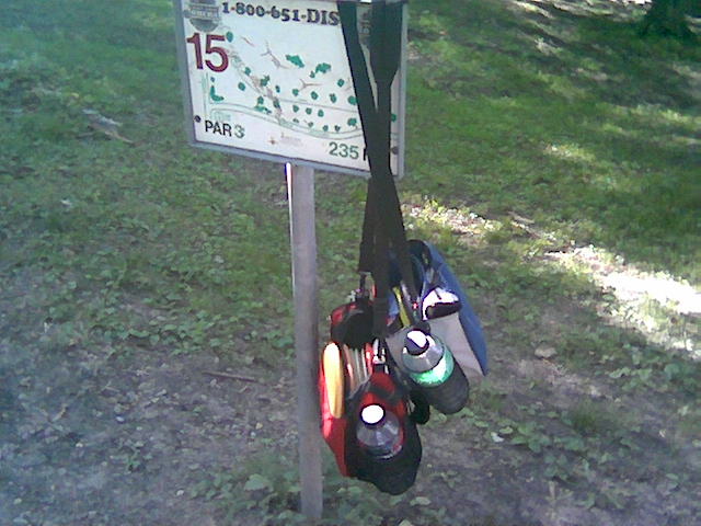 Disc golf bags hang from a signpost for hole 15
