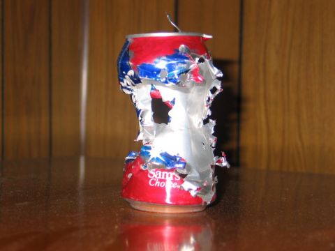 2004 Ford F-150 - A severely damaged aluminum can sits on a reflective surface against a wood-paneled background.