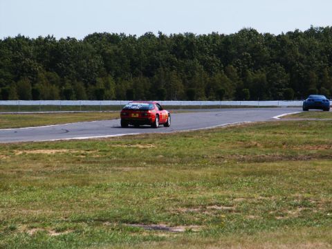 2001 Mercury Grand Marquis - Two cars on a race track with trees and a fence in the background.