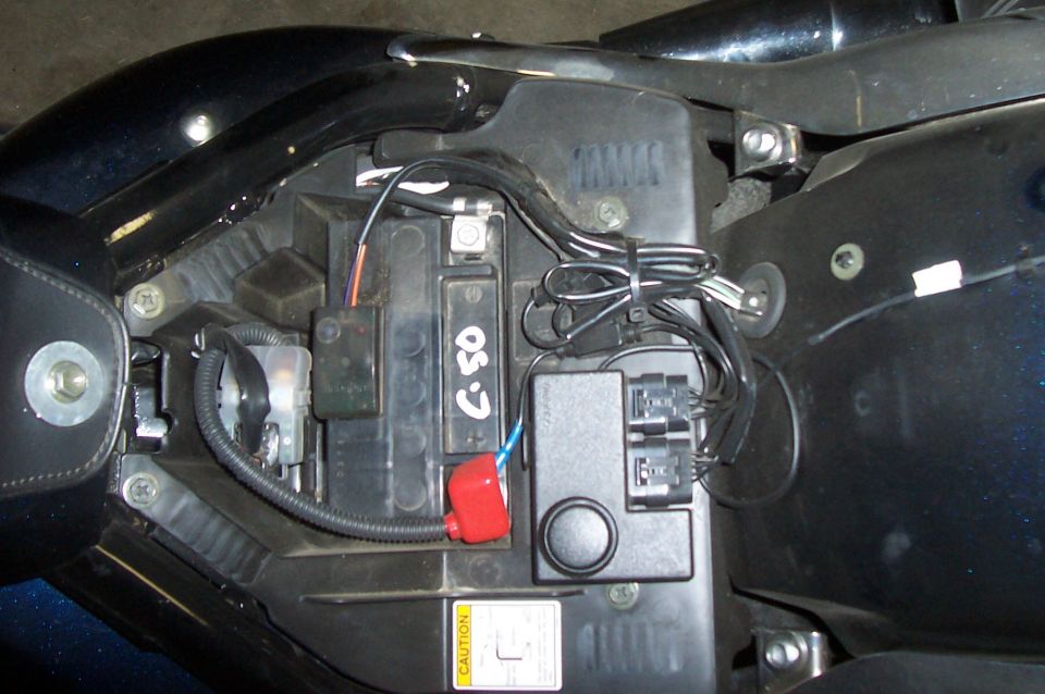 Motorcycle battery with visible wiring, fuses, and a red terminal cover