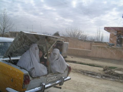 1979 Ford Bronco - Three women in burqas are seated in the open trunk of a yellow car, with a fourth person visible in the front seat.