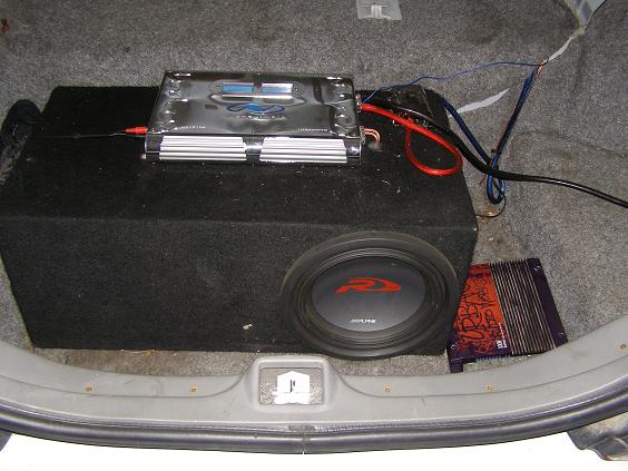 Car trunk interior with a large subwoofer box, amplifier, and wiring