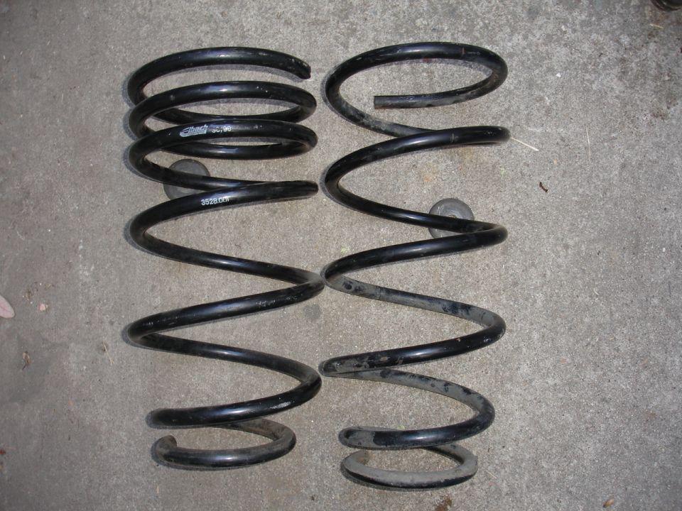 Two black coil springs, one with text '3528 CR' visible, lying on a concrete surface