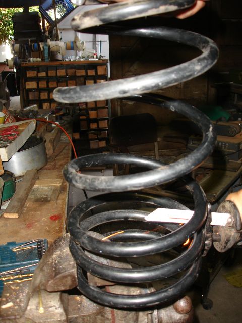 1995 Ford Taurus - A black coil spring is clamped in a vise, with tools and a workbench visible in the background.