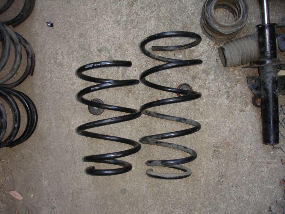 Two black coil springs and a strut assembly on a concrete surface