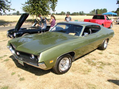 1967 Ford Ranchero - A green 1970 Ford Torino coupe is parked at an outdoor car show, with a black car with its hood open behind it.