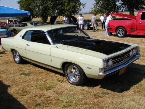 1967 Ford Ranchero - A cream 1969 Ford Torino with a black hood and racing stripes is displayed at an outdoor car show.