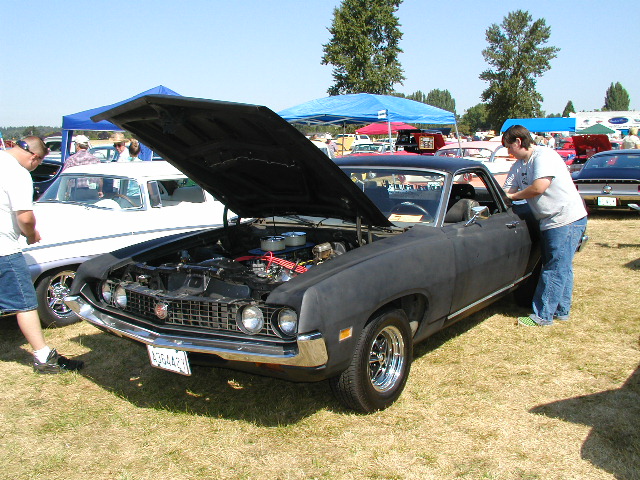 Black 1968 Ford Ranchero with hood open, chrome wheels, and a person by the door