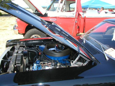 1967 Ford Ranchero - The engine bay of a black Ford Falcon is visible, with a red pickup truck behind it.