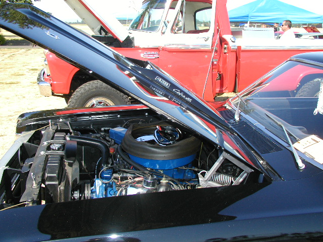 Black Ford Falcon with hood open, showing engine. Red pickup truck in background