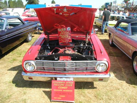 1967 Ford Ranchero - A red 1963 Ford Falcon Futura is displayed with its hood open at a car show, alongside other vehicles.
