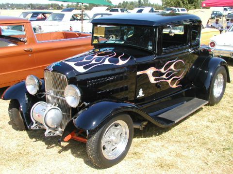 1967 Ford Ranchero - A black coupe with flame graphics is displayed at an outdoor car show, with other vehicles visible in the background.