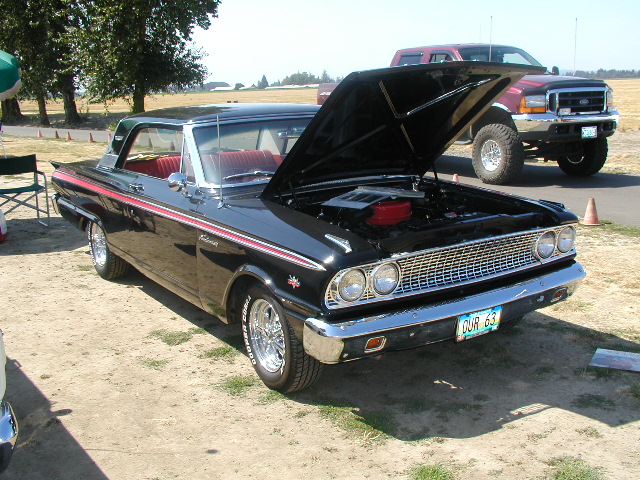 Black 1963 Ford coupe with red interior, hood open, chrome grille, and dual headlights