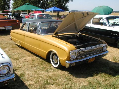 1967 Ford Ranchero - A yellow sedan, possibly a Ford Falcon, is displayed with its hood open at an outdoor event.