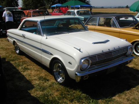 1967 Ford Ranchero - A white 1963 Ford Falcon coupe is parked on grass at a car show, with other vehicles visible in the background.