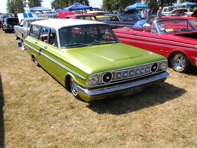 Lime green station wagon with a white roof, parked on dry grass next to a red convertible