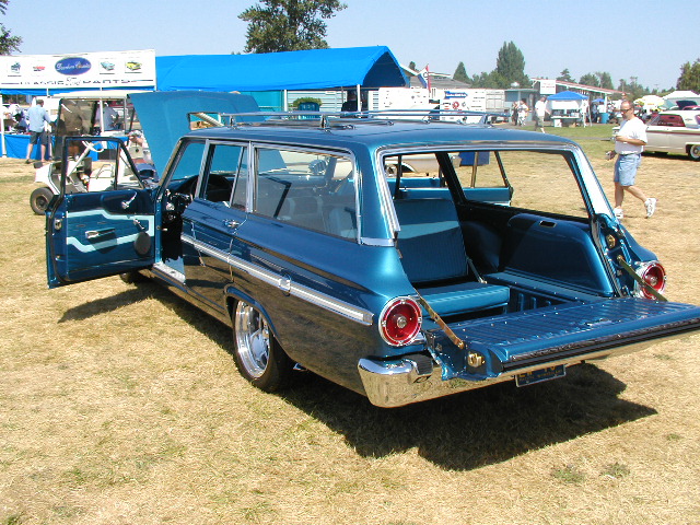 Teal 1960s Ford station wagon at a car show with tailgate down and rear door open