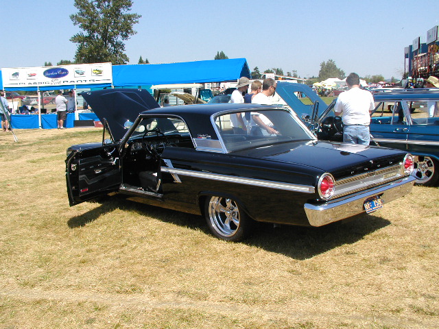 Black 1963 Ford Galaxie 500 with doors and hood open, parked on grass next to a blue station wagon