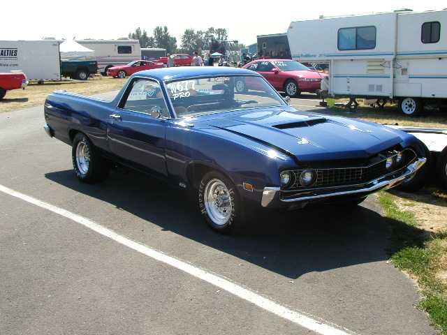 Blue Ford Ranchero with hood scoop and drag slicks staged on pavement at a race event
