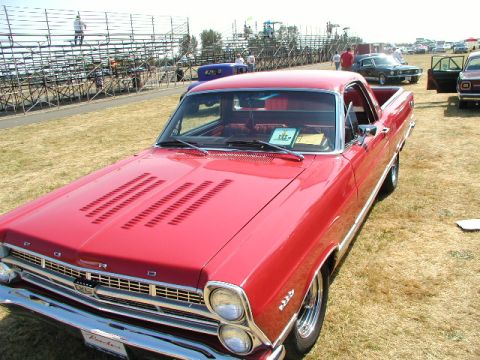 1967 Ford Ranchero - A red 1967 Ford Ranchero is displayed at a car show, with other vehicles and spectators visible.