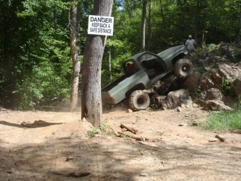 1974 Ford Bronco - Off-road truck navigating a challenging rocky terrain, with a safety warning sign posted nearby.