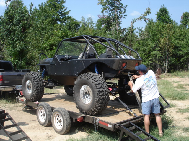 Custom black off-road buggy with roll cage on a trailer, being secured by a man