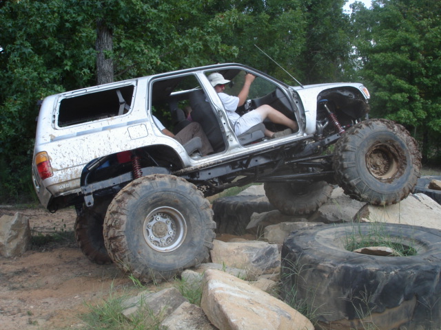 Silver SUV modified for off-roading, with large tires and lifted suspension, navigating rocks