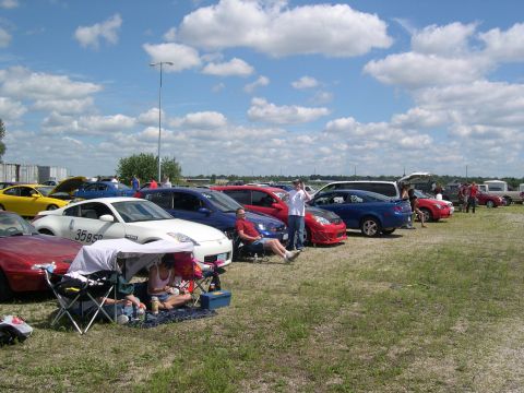 2002 Ford Focus - A variety of cars are parked on a grassy field on a sunny day with scattered clouds.