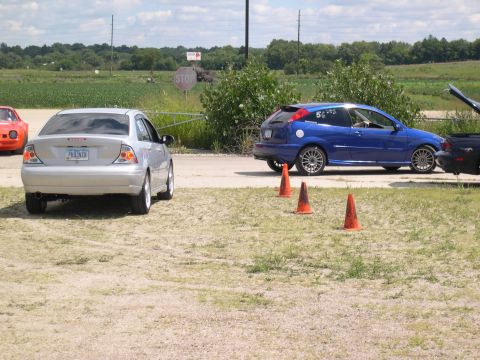 2002 Ford Focus - A silver sedan and a blue hatchback are parked on a dirt lot, with orange cones marking a path.