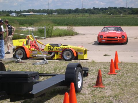 2002 Ford Focus - Two race cars are on an asphalt track with orange cones and grassy areas.