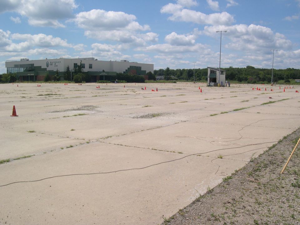 Empty paved lot with orange cones set up, building in background