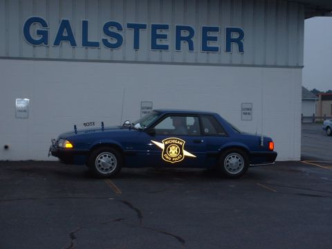 1978 Ford Mustang II - A blue Michigan State Police car is parked in front of a building with 'GALSTERER' signage.
