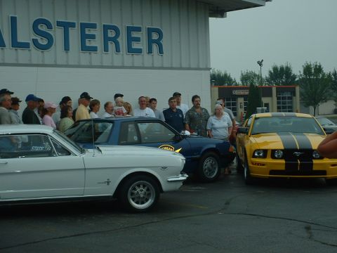 1978 Ford Mustang II - A yellow and black striped Ford Mustang is parked in front of a building with a crowd of people.