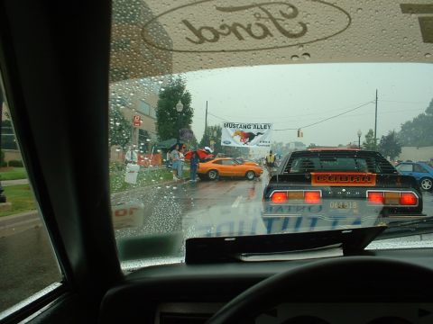 1978 Ford Mustang II - A black Ford Mustang Cobra is visible through a rain-streaked windshield, parked on a street with other cars.